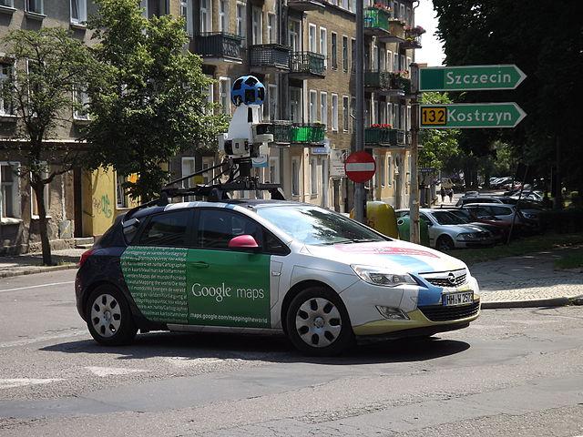 Small sedan with large camera mounted on top, driving down a street in a European country.